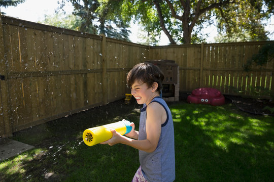 Playful boy using squirt gun in sunny backyard
