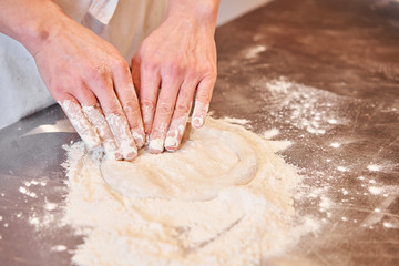 Dough for Neapolitan pizza, the chef rolls out the blanks. Closeup hand of chef baker in uniform white apron cook pizza at kitchen