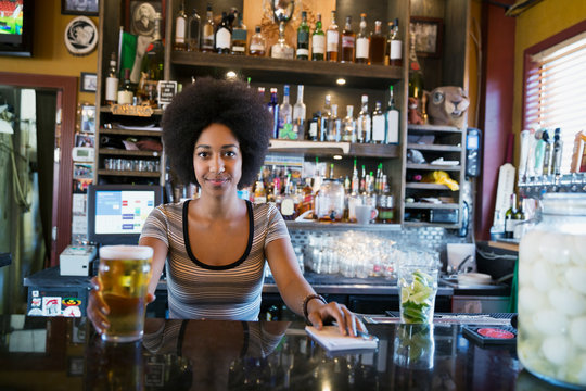 Portrait confident female bartender serving beer behind counter