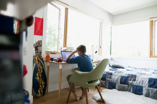 Boy with head in hands using laptop in bedroom