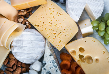 different assortment of cheeses with fruits and nuts is on the cutting Board