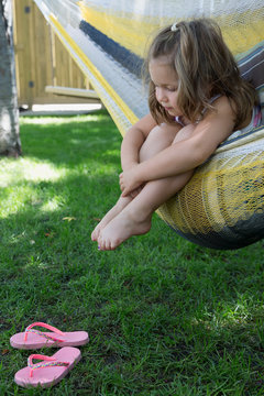 Girl dangling bare feet over hammock in backyard