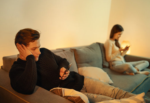 Smartphone Addicted Couple Use Phones Sit On Sofa At Home, Overuse Social Media, Internet Addiction Concept. Bored Distant Young Couple Ignoring Each Other.