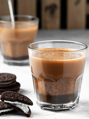 Two glasses of coffee with milk, next to chocolate cookies. Coffee is located on a light gray background. Close-up, vertical orientation. Shallow depth of field. Breakfast or snack concept
