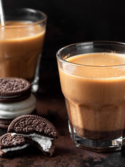 Two glasses of coffee with milk, next to chocolate cookies. A glass of cold drink is located on a dark metal background. Close-up, vertical orientation. Shallow depth of field.