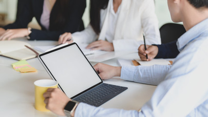 Cropped shot of businessman with blank screen tablet while working with team in co working space