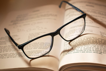 Pair of reading glasses on an opened book, with beautiful shadows falling on the words.