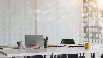 Cropped shot of co working space with laptop, office supplies, and coffee cup on white desk with blurred office room