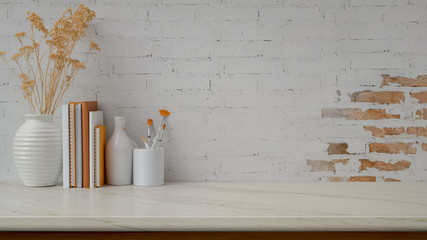 Cropped shot of workspace with copy space, vases, paint brush and books on marble desk with  brick...