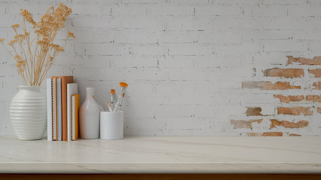 Cropped shot of workspace with copy space, vases, paint brush and books on marble desk with  brick wall