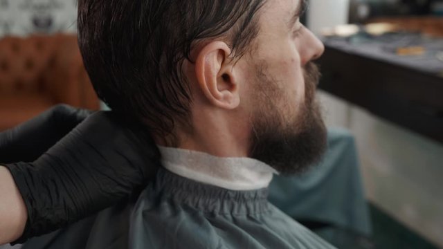 Barber putting on mantle before haircut to bearded man in male salon. Hairstylist working with client in barber shop. Male hair care in barber salon