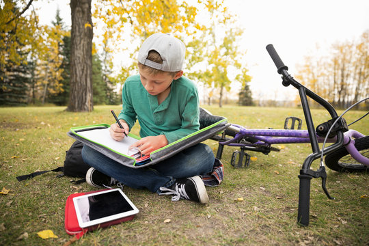 Tween boy doing homework in autumn park