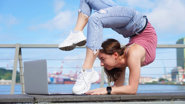 beautiful flexible girl stands in a bridge in front of a laptop on a viewing platform near the port. Lifestyle girl working on a journey. Backbend pose.