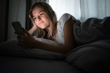 Pretty, young woman in her bed with her cell phone, waking up using a sleep monitoring app. Smartphone in Bed Mobile/smartphone  Addiction Concept.