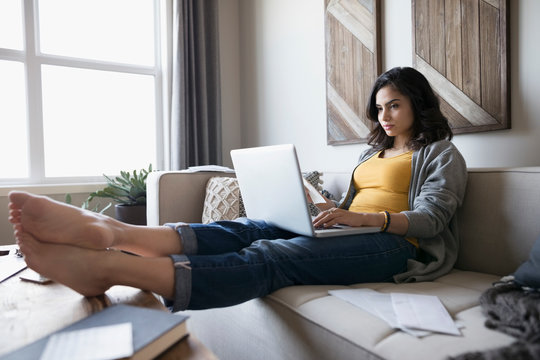 Young Woman With Laptop Paying Bills Online On Living Room Sofa