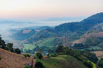 Obraz premium View of village and mountain covered in foggy during morning sunrise.