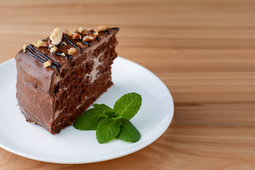 Sweet chocolate cake with walnuts and frosting on top served on a white plate on light wooden background. Copy space.
