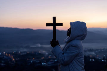 Silhouette human praying and holding christian cross for worshipping God at sunset background.Christian, Christianity, Religion copy space background.