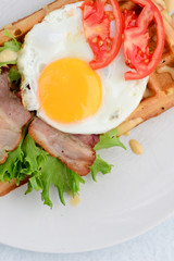 Classic eggs and bacon meat on waffles breakfast with tomatoes and salad served on a white plate on white background.