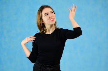 Fototapeta premium Studio portrait of a pretty blonde girl in a black T-shirt on a blue background with bright emotions. A universal concept, the picture is suitable for any topic.