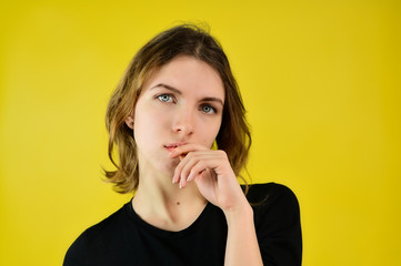 Close-up Studio portrait of a pretty blonde girl in a black T-shirt on a yellow background with bright emotions. A universal concept, the picture is suitable for any topic.