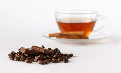 Glass cup of tea with cinnamon sticks, coffee beans and chocolate. White background. Isolated. Hot spiced cinnamon tea. Blurred background.