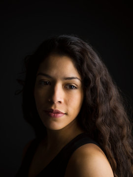 Portrait pensive Latina woman with long curly hair looking over shoulder against black background