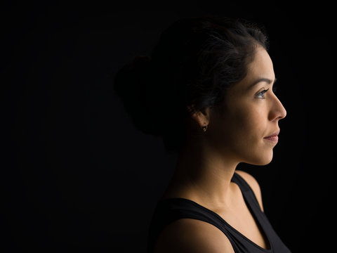 Profile portrait serious, pensive Latina woman looking away against black background
