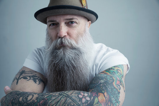 Portrait Caucasian male hipster with long gray beard and arm tattoos wearing fedora