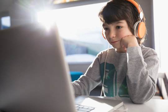 Pre-adolescent boy wearing headphones listening to music at laptop