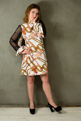 Model stands near a concrete wall. Full-length studio portrait of a pretty blonde girl in bright dress on a gray background.