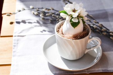 Sunny Easter composition of willow branches and natural flowers in a white egg in a circle on a gray tablecloth.