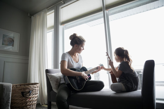 Daughter with ukulele watching mother playing guitar in living room