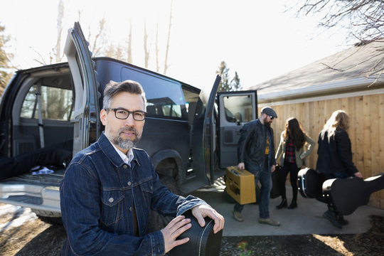 Portrait Confident Male Music Band Musician With Guitar Case Outside Van In Sunny Driveway