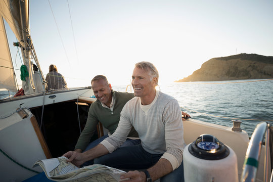 Senior men viewing map on sunset sailboat