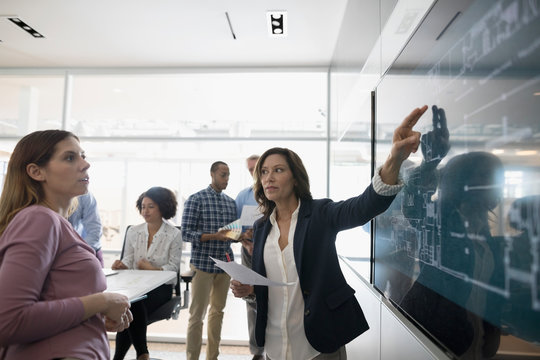 Female Architects Discussing Digital Blueprints At Screen In Conference Room Meeting