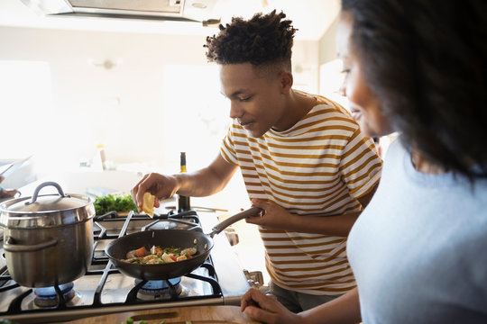 African American mother and teenage son cooking at stove in kitchen