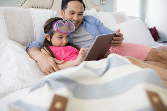 Father and daughter wearing goggles using digital tablet on bed