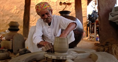 Skilled professional potter throwing the potter's wheel and shaping traditional ceramic vessel and clay ware: pot, jar in pottery workshop. Handwork craft from Shilpagram, Udaipur, Rajasthan, India