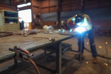 Isolated arc welder using earth clamp on the side table with defocused welder performing welding steel bolts into the metal plate at the construction fabrication site workshop 