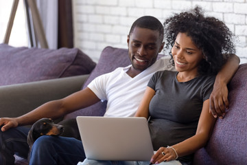 Happy black couple relax with dog watching movie on laptop