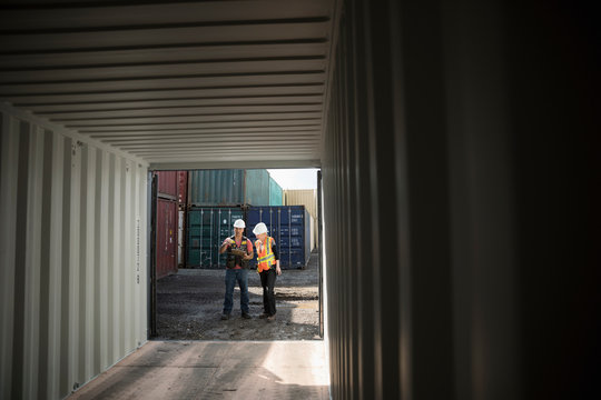 Workers inspecting empty shipping container in industrial container yard