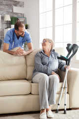 Obraz premium Old woman sitting on couch holding her crutches