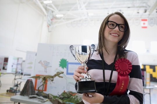 Portrait smiling, confident girl middle school student holding trophy and wearing champion prize ribbon at science fair