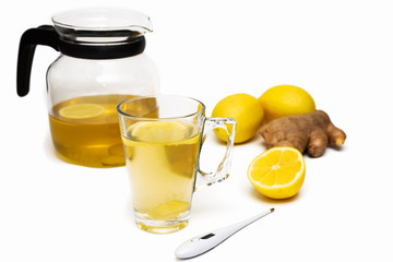 Transparent teapot and mug of herbal tea, lemons, ginger, thermometer on white background. Cold and flu season. Alternative medicine concept. Natural remedies. Copy space