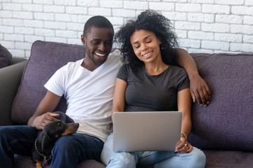 Happy black couple using laptop relaxing with pet at home