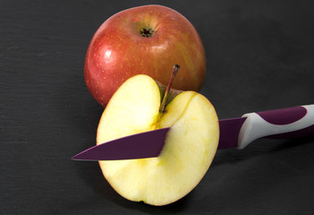 Manzana junto a media cortada y atravesada por un cuchillo.