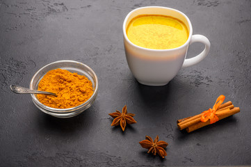 Glass cup of traditional indian masala chai tea with ingredients above. Cinnamon, cardamom, anise over dark texture background