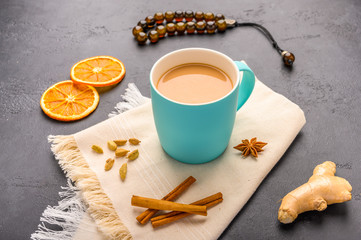 Traditional Indian masala tea chai with milk and spices on napkin on dark stone background with ingredients above