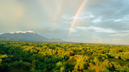 Obraz premium Rainbows over a farm in the mountain. Aerial shot.